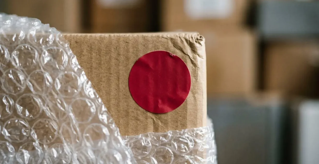 Détail d'un autocollant fragile rouge apposé sur carton avec objets délicats emballés